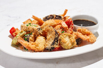 Shrimp and vegetable tempura, served with dipping sauce, on a white plate