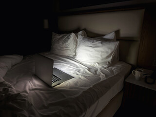 Laptop on hotel bed at night with soft light, empty bedroom interior showing late work, remote lifestyle or insomnia concept, quiet modern hotel room with technology and solitude © Evgeniia Primavera