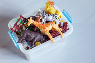 Plastic animal toys in storage box, Assorted plastic animal toys in a white storage box, including zebra, giraffe, tiger, and rhino figures, representing childhood play, learning, and imagination