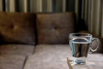 Clear glass of water on a table in front of a sofa, creating a warm and simple home atmosphere...