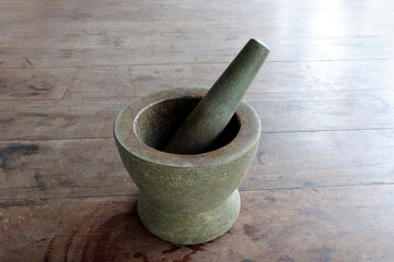 Traditional stone mortar and pestle on a wooden floor. Thai kitchen utensil used for grinding chili, herbs, spices, and preparing authentic Asian food