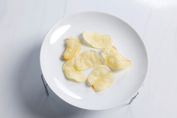 Thin crispy potato chips arranged on a white plate, Crispy potato chips on plate in bright studio lighting, showing texture and simple minimal food presentation