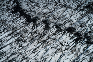 Aerial view of a glacier in Iceland showing striking natural patterns, cracks, and dark volcanic ash layers