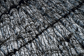 Aerial view of a glacier in Iceland showing striking natural patterns, cracks, and dark volcanic ash layers