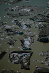 Chunks of glacial ice covered with volcanic ash floating in milky meltwater. A surreal aerial view from Iceland capturing the effects of melting glaciers and the planet&rsquo;s changing climate