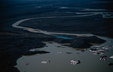 Top-down abstract view of dark glacial ice blocks drifting on muddy lake water in Iceland. The natural geometry of melting ice and volcanic ash creates a fine art composition