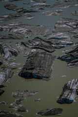 Chunks of glacial ice covered with volcanic ash floating in milky meltwater. A surreal aerial view from Iceland capturing the effects of melting glaciers and the planet&rsquo;s changing climate