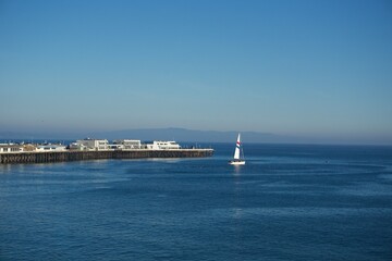 Single sailboat sailing near Santa Cruz Wharf on calm Pacific Ocean waters