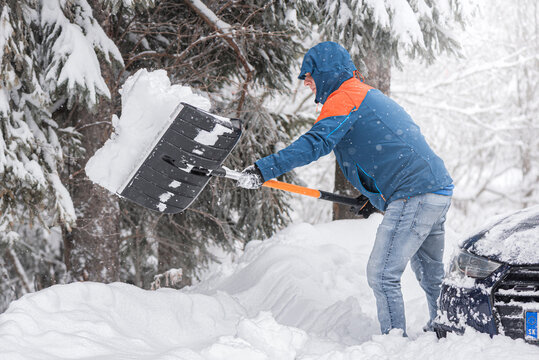 Clearing snow from a car stuck in a snowdrift using a shovel.