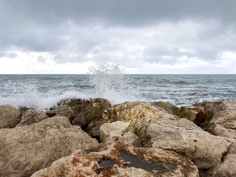 Mediterranean waves crashing against rocky shore under dramatic storm clouds in Oliva Spain