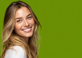 Fototapeta premium Lächelnde blonde Frau mit weißem Top vor grünem Hintergrund strahlt Fröhlichkeit aus