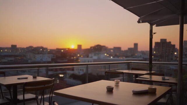 A serene rooftop restaurant patio with tables and chairs overlooking a city skyline during a warm sunset 