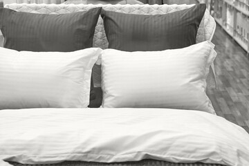 Comfortable bedding display with white and dark pillows on wooden flooring in a cozy bedroom...