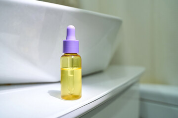 Yellow glass dropper bottle with purple cap on bathroom counter for skincare and beauty product...