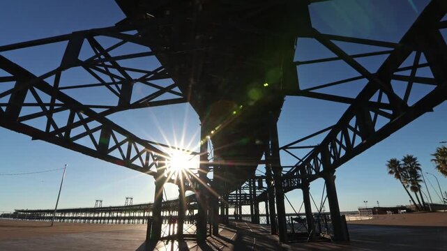 Spectacular low angle sunburst view through the massive iron framework of the Muelle del Rio Tinto, capturing the industrial silhouette against a bright blue sky.