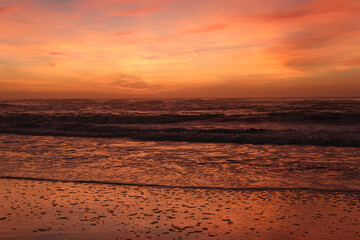 Dramatic orange sunset over ocean waves reflecting on wet sandy beach