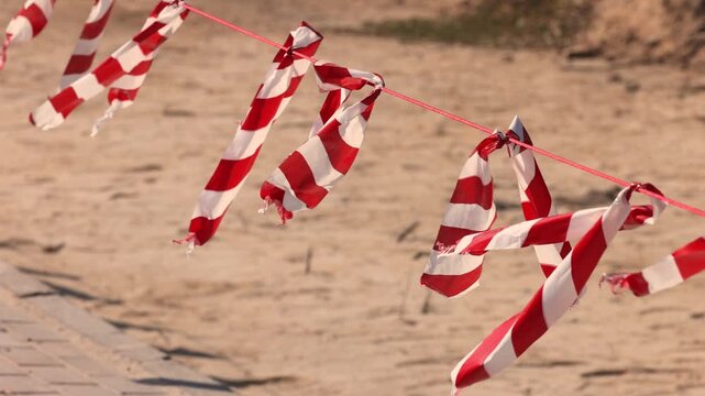Red white plastic safety barrier tape tied to rope marking dangerous area zone
