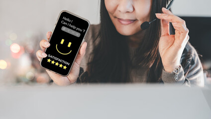 Asian woman using headset and showing smartphone with satisfaction rating screen, representing CRM service, customer support, online consulting, legal aid, or friendly communication assistance.