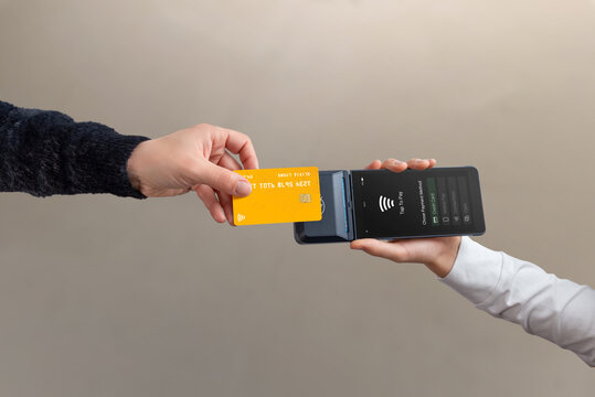 Contactless credit card tap to pay on mobile POS terminal held by cashier, showing modern wireless payment and digital checkout process