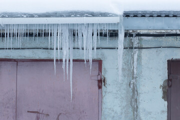 Icicles are hanging from the roof of the house. Winter landscape.