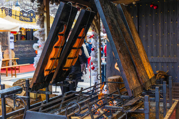 Thick salmon fillets are cooked vertically over an open wood fire at a food stall, with white festive garland in the foreground, at the Budapest Christmas Market, Hungary, December 2025
