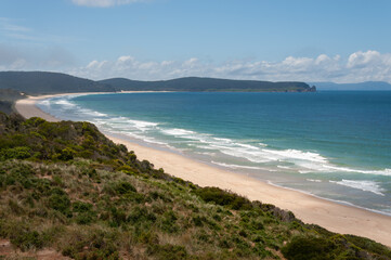 Obraz premium Bruny Island coastal landscape with long sandy beach, gentle waves and green hills, showing remote Tasmanian shoreline and natural ocean environment.