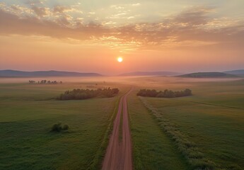 Fototapeta premium Aerial view of serene countryside landscape with dirt road at sunrise, rolling hills and misty fields.
