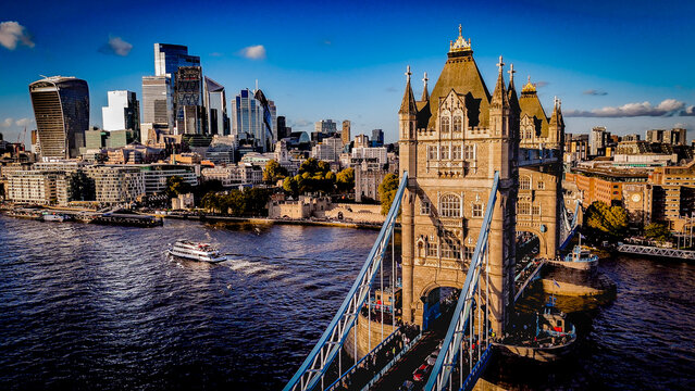Tower Bridge captured from a low-angle perspective under clear blue skies, highlighting its iconic architecture and the modern London skyline in warm afternoon light.
