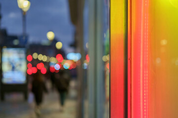 Street at dusk or night, focusing on the vibrant red and yellow neon lights of a storefront contrasted with a blurred street scene in the background. selective focus