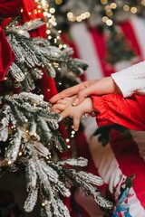 A close-up photo of a mother and daughter's hands, a child, and a woman near a Christmas tree, searching for a gift. New Year's holiday concept.