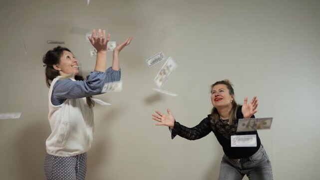 Two women happily catches money up in the air inside of a house during the daytime