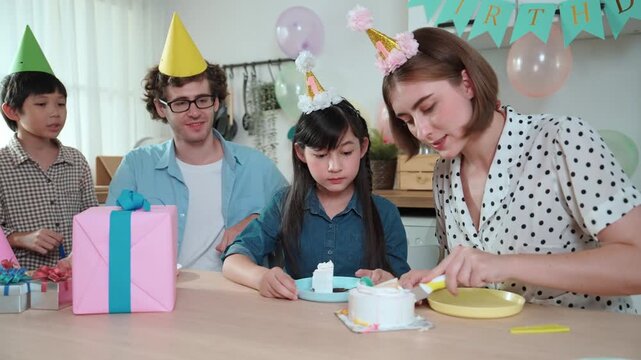 Caucasian mom cutting birthday cake and separated dessert while give to father. Happy family wear party hat to celebrated daughter birthday while sitting at table. Special occasion concept. Pedagogy.