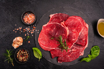 Raw organic steak with ingredients for cooking on a dark slate, stone or concrete background. Top view with copy space. High quality photo
