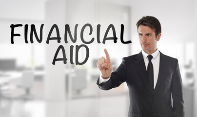 Professional businessman in a dark suit points at the words financial aid on a transparent screen, with a bright blurred modern office interior in the background. 