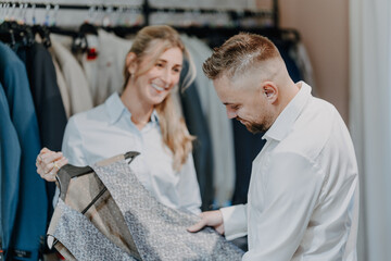 Professional tailor assisting a male customer choosing a stylish vest and suit inside a modern menswear boutique with friendly service and quality fashion