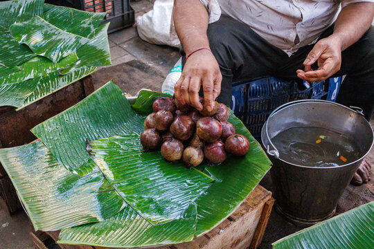 Indian street vendor arranging fresh jamun (java plum) fruits on banana leaves at a traditional market stall.