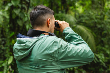 Rear view of male tourist using binoculars to observe wildlife in Monteverde rainforest