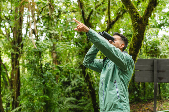 Young male birdwatcher pointing and using binoculars in Monteverde Cloud Forest Costa Rica