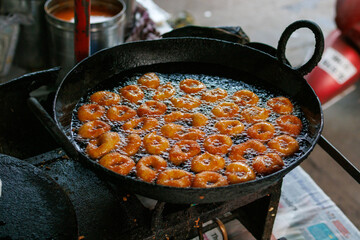 Traditional Indian sweet vada frying in hot oil in black iron pan at street food stall