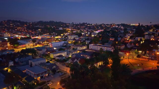 A dramatic aerial view at night captures the brilliant, illuminated skyline of downtown Los Angeles reflecting across the dark, placid surface of Echo Park Lake