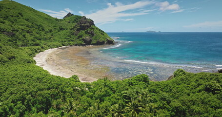 Fiji, Kuata island: secluded tropical beach with crystal clear blue water lagoon lapping against lush greenery mountain hill and a rugged coastline. Drone flight shows wild nature beauty