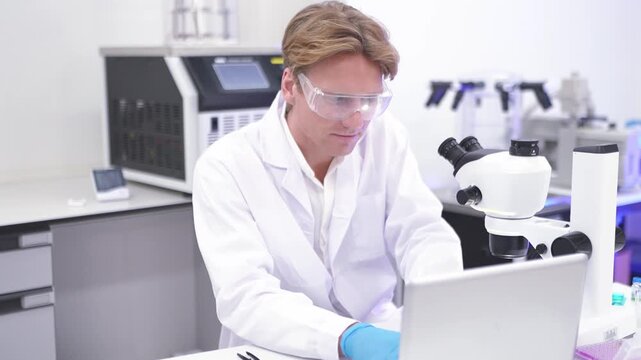 Scientist studies samples in lab with microscope and computer