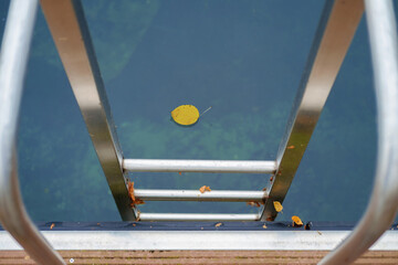 Metal handrail for descent into the lake, pier on the lake and calm lake water on background, selective focus