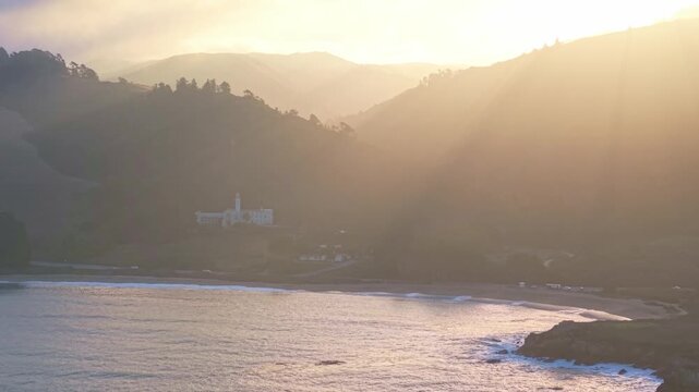 The historic Carmelite Monastery is captured overlooking Monastery Beach and the Pacific Ocean in a serene aerial view bathed in morning sunlight