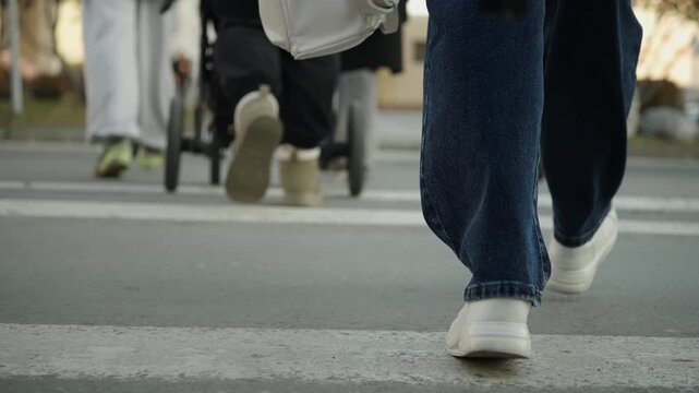 Close-up sequence of white sneakers and denim jeans walking across an urban crosswalk, from first to last frame, capturing pedestrian movement on a city street from a low-angle perspective.