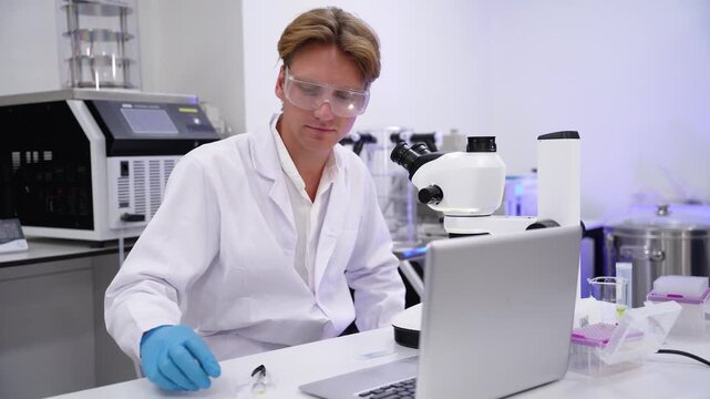 Scientist examines samples at laboratory using microscope and computer