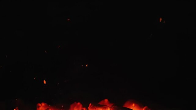 Glowing Embers on Black - A close-up shot showcases a pile of hot embers glowing with an orange hue against a dark background. Specks of light or embers float in the air above the pile.