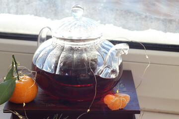 A transparent teapot with black tea sits on the windowsill. There's snow outside. It's December.