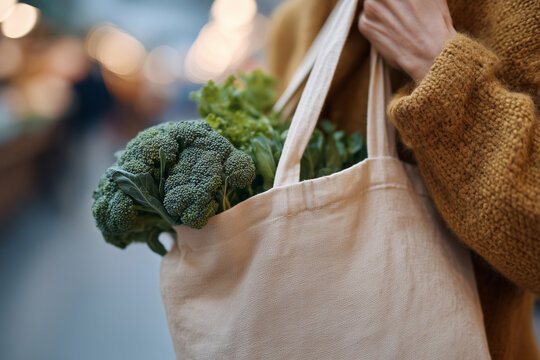 A woman is holding a bag of vegetables, including broccoli and spinach