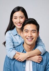 Happy young asian couple portrait on a grey background. Affectionate woman hugging her smiling partner from behind. Love and relationship concept